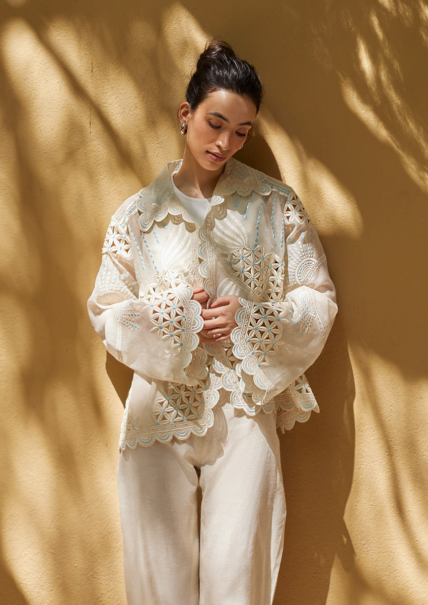 A model showcases Nainpreet Edit '25 Ayla: an ivory organza top with intricate cutwork, scalloped edges, and pearl details suitable for Indian festive wear.